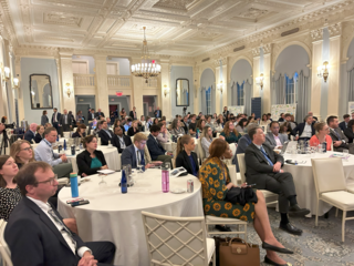 Photo of the audience at tables listening to the panel. 